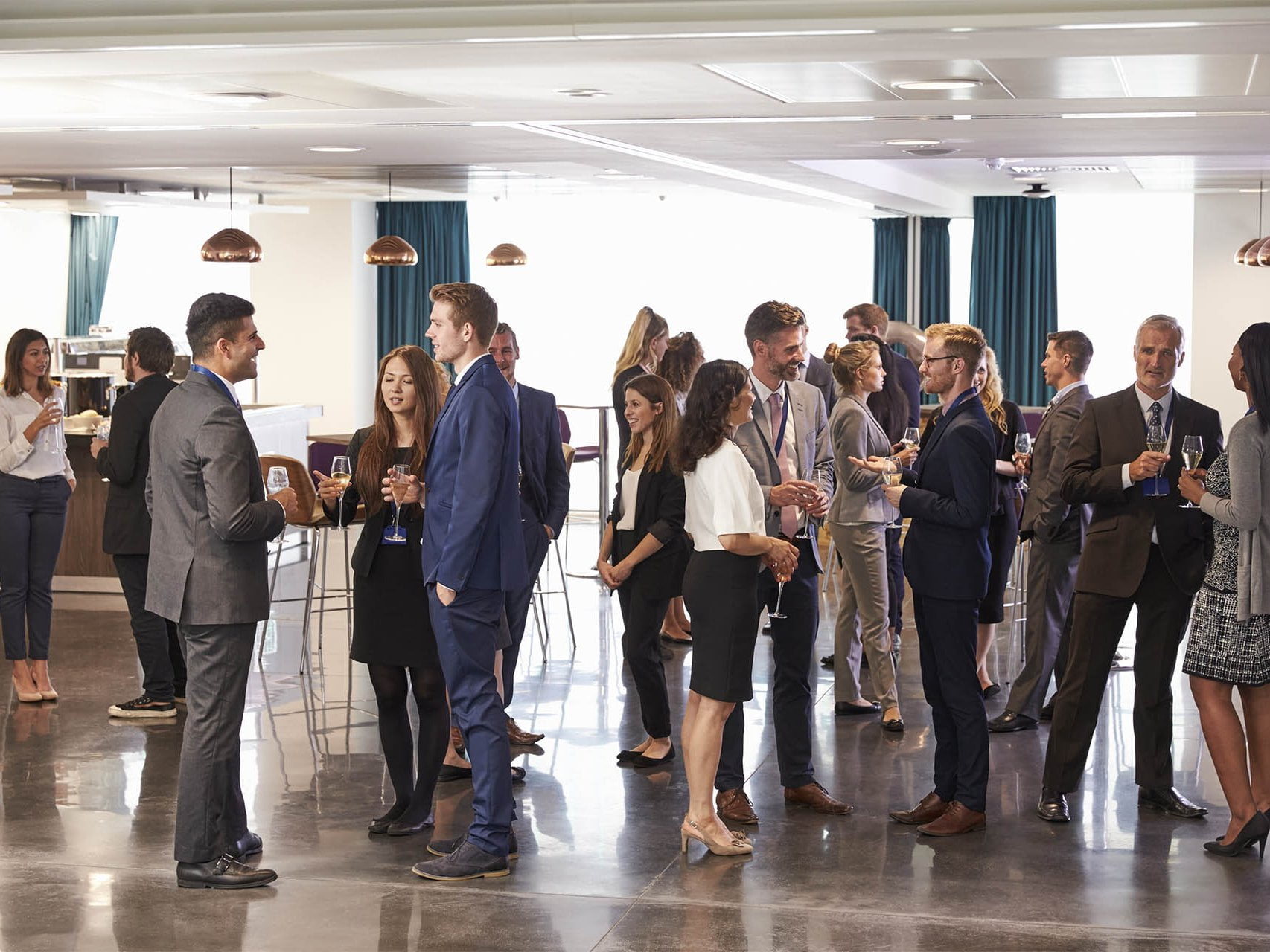 A photo of a cafeteria hosting a networking event filled with business men and women mingling together with drinks. This is an image relating to the blog article: Five tips for attending networking events