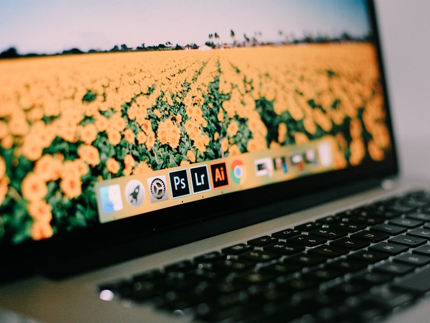 A close up photo of an Apple Macbook laptop, focused on the bar with three active applications, Adobe Photoshop, Adobe Lightroom, and Adobe Illustrator. This is an image relating to the tutorial article: How to resize multiple images in Photoshop at once.
