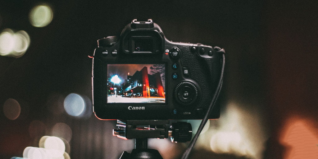 A close up photo of a camera from the operators view, attached to a tripod, set to photograph a building during the night. This is an image relating to the blog article: Why video belongs in your content marketing plan